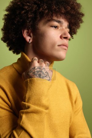 Foto de Crop ethnic guy with Afro hairstyle wearing yellow turtleneck and looking pensively away on green background - Imagen libre de derechos