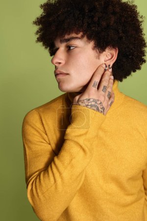 Photo for Pensive male model in yellow turtleneck and with Afro hairstyle touching neck on green background - Royalty Free Image