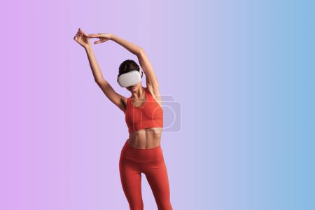 Téléchargez les photos : Femme mince anonyme en vêtements de sport et casque VR étirant les bras tout en se tenant debout sur fond violet dégradé - en image libre de droit