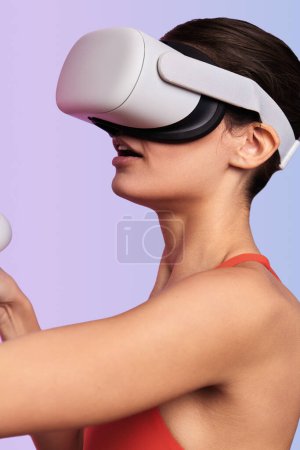 Téléchargez les photos : Vue latérale de la jeune femme en lunettes VR interagissant avec la réalité virtuelle sur fond violet. Plan vertical - en image libre de droit