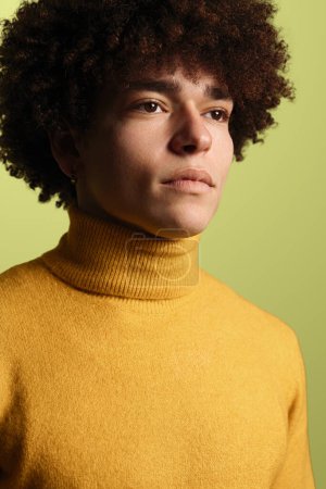 Foto de Modelo masculino joven serio con peinado afro en suéter amarillo mirando hacia otro lado sobre fondo verde. Retrato vertical - Imagen libre de derechos