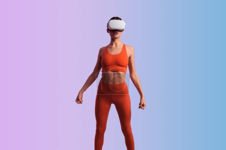 Téléchargez les photos : Jeune femme en tenue de sport rouge et lunettes VR faisant de l'exercice de roulis d'épaule avec des poings serrés pendant l'entraînement de remise en forme sur fond dégradé - en image libre de droit