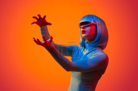 Téléchargez les photos : Jeune femme futuriste en perruque formant boule invisible avec les mains sur fond orange - en image libre de droit