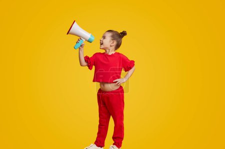 Photo for Excited kid leader speaking in megaphone and smiling while standing against yellow background. Young leader concept - Royalty Free Image