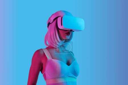 Foto de Mujer joven futurista en gafas VR en realidad virtual sobre fondo azul - Imagen libre de derechos