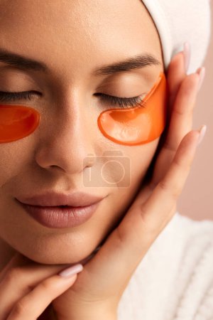 Photo for Crop face of young female touching face while applying eye patches and relaxing after taking shower - Royalty Free Image