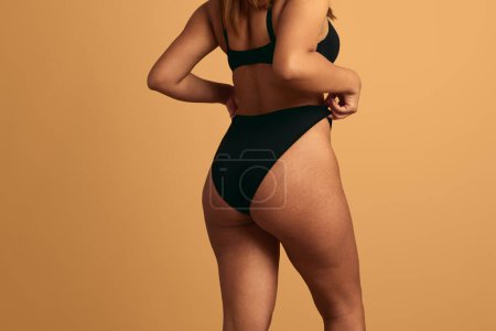 Foto de Vista posterior de la cosecha anónima mujer de talla grande en lencería negra demostrando nalgas sobre fondo marrón - Imagen libre de derechos