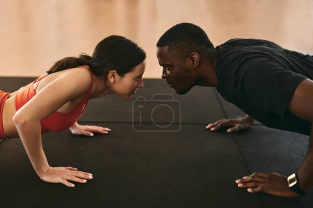 Photo for High angle side view of fit lady and black guy doing plank exercise on mat against each other while competing in gym - Royalty Free Image
