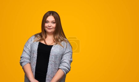 Téléchargez les photos : Plus la taille jeune femme en tenue décontractée regardant la caméra avec un espace de copie sur fond jaune - en image libre de droit
