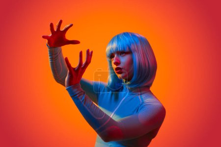 Téléchargez les photos : Jeune femme futuriste en tenue cybernétique contrôlant l'interface virtuelle avec des gestes de mains contre la lumière vive au néon - en image libre de droit