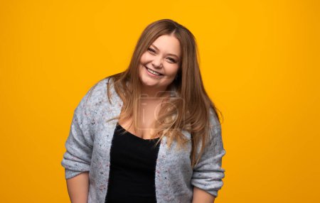 Photo for Happy plus size young female in casual outfit smiling and looking at camera while standing on yellow background - Royalty Free Image