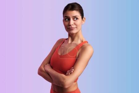 Photo for Young slim female in red sportswear with funny face expression crossing arms in studio against gradient background looking away - Royalty Free Image