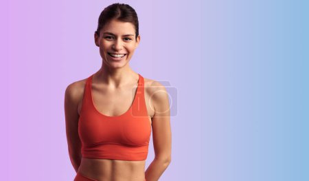Foto de Joven atleta positiva en ropa deportiva sonriendo y mirando a la cámara mientras está de pie sobre fondo violeta - Imagen libre de derechos