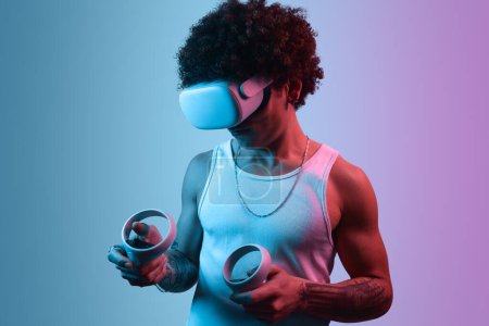 Foto de Hombre étnico en gafas VR y con controladores jugando videojuego contra fondo violeta - Imagen libre de derechos