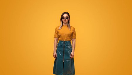 Photo for Full length young female in trendy cyberpunk outfit touching neck while standing against yellow background - Royalty Free Image