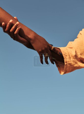 Téléchargez les photos : Angle bas de culture anonyme homme africain tenant la main de sa petite amie portant des anneaux contre le ciel sans nuages dans l'amour de la lumière du soleil et concept d'unité - en image libre de droit