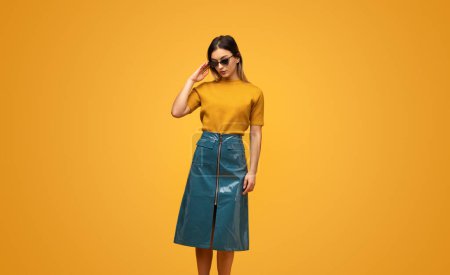 Téléchargez les photos : Jeune femme confiante en tenue tendance et lunettes de soleil debout sur fond jaune - en image libre de droit