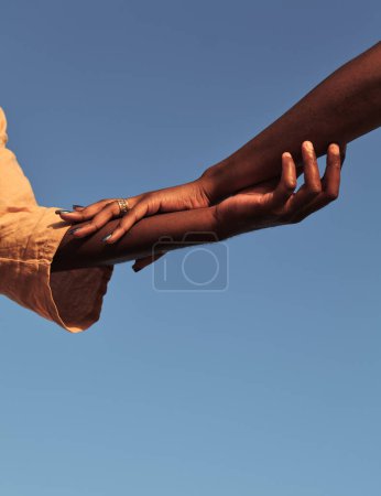 Foto de Bajo ángulo de pareja africana acariciándose las manos contra el cielo azul sin nubes a la luz del sol en verano - Imagen libre de derechos