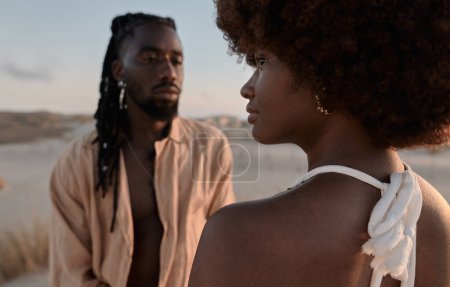 Foto de Joven mujer africana con cabello afro de pie delante de su novio con rastas en la costa arenosa al atardecer durante la noche de verano - Imagen libre de derechos
