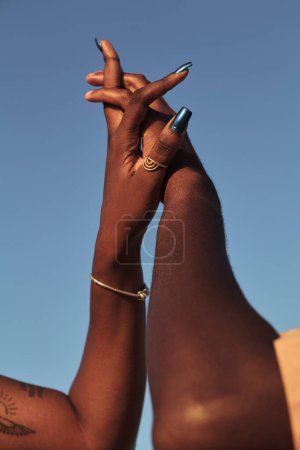 Foto de Bajo ángulo de pareja africana entrelazando las manos contra el cielo azul sin nubes en la unidad del día soleado y el concepto de amor - Imagen libre de derechos