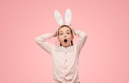Photo for Bright little girl with braids and in bunny ears holding hands on head and screaming at camera in excitement - Royalty Free Image