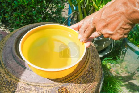 Hand hält Wasserdipper gelb auf thailändischem Glasbehälter Hintergrund.