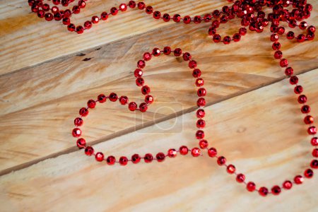 Photo for The heart is lined with red beads on a wooden table. A heart is lined with beads on the table. Valentine's Day - valentine on the table with your own hands. - Royalty Free Image