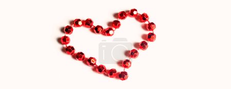 Téléchargez les photos : The heart is lined with red beads on a wooden table. A heart is lined with beads on the table. Valentine's Day - valentine on the table with your own hands. - en image libre de droit