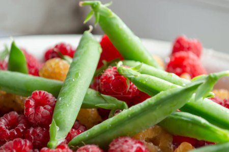 Photo for Fresh, summer berries - green peas in pods and red raspberries. Green peas are in the same bowl with red raspberries. Healthy legumes are in the summer. - Royalty Free Image