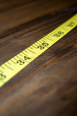 Photo for On a wooden background is a yellow meter for a seamstress. A meter for measuring volume and height is on the table. - Royalty Free Image