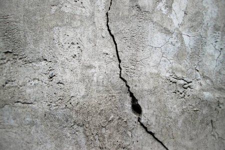 Vertical crack on the wall with a hole. Concrete old surface with grainy texture.