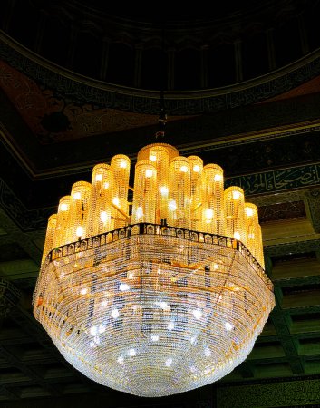 Old Style huge lantern hanging in the dome of Islamic architechture with golden shining lights and dark backdrop.