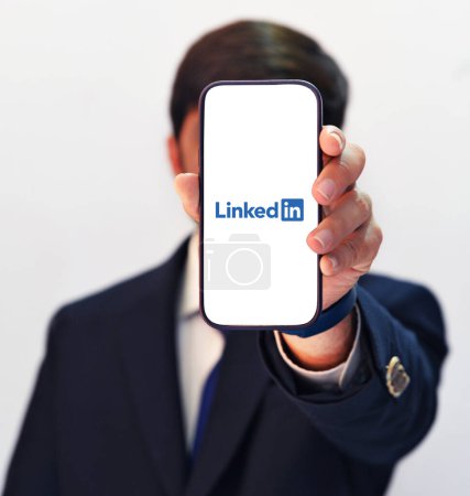 Téléchargez les photos : Suited Man montrant LinkedIn Application ouverte sur mobile, fond de technologie éditoriale. Emploi hanter ou embaucher arrière-plan plate-forme - en image libre de droit