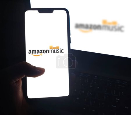 Téléchargez les photos : Personne utilisant l'application mobile d'AmazonMusic sur smartphone avec écran blanc isolé, fond éditorial - en image libre de droit