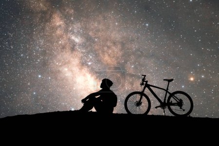 Foto de Silueta de un ciclista sentado y mirando una Vía Láctea - Imagen libre de derechos