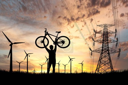 Téléchargez les photos : Silhouette d'homme et vélo au coucher du soleil. éoliennes en arrière-plan - en image libre de droit