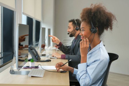Foto de Los auriculares femeninos afroamericanos felices del desgaste están trabajando en un centro de llamadas, agentes del operador de la gente de negocios que contestan el teléfono en línea - Imagen libre de derechos