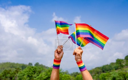 Téléchargez les photos : Personnes main tenant lgbt coloré arc-en-ciel drapeau gay fond ciel bleu sur l'été, concept de diversité lgbtq genres amour, activiste, droits, protestation, défilé de mouvement, célébrer, festival, heureux mois de la fierté - en image libre de droit