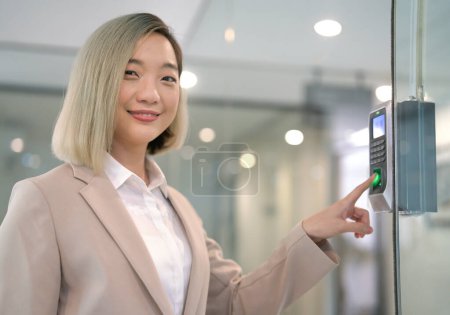 Téléchargez les photos : Une jeune employée souriante utilisant un capteur de pression d'index pour une fréquentation record - travail à l'entreprise - en image libre de droit