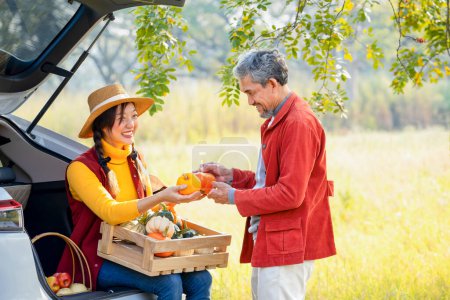 a mature man,agricultural product middleman talking and checking the quality of the fruit before deciding to buy from a young woman gardener that sitting in the back of a car in her farmland in autumn
