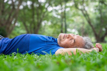 sportlicher älterer Mann legt sich auf Rasen und macht ein Nickerchen während er sich im Park ausruht, ausreichend Schlaf am Tag hilft dem älteren Körper, sich auszuruhen und Kraft zu tanken, um die täglichen Aktivitäten normal auszuführen