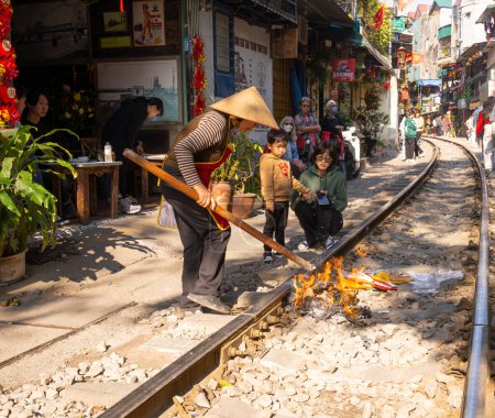 Photo for Hanoi, Vietnam. January 2023. A woman burning tien am phu, votive offerings for ancestors along the train tracks in front of her home in the old quarter of the city - Royalty Free Image