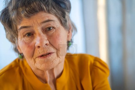 Das Porträt einer lachenden, lächelnden älteren Frau mit grauen Haaren und Falten im Gesicht, aber jung im Herzen und einem aktiven Lebensstil. Glückliche Rentnerin posiert in ihrem gemütlichen Zuhause.