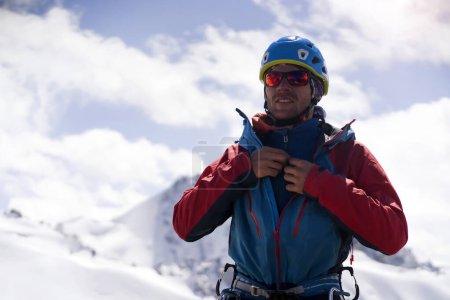 Photo pour Un homme en lunettes d'alpinisme spéciales avec une couleur orange effet miroir, prend soin de sa vue et de la sécurité dans les montagnes enneigées. Le randonneur voyage dans les montagnes, est engagé dans l'escalade. - image libre de droit