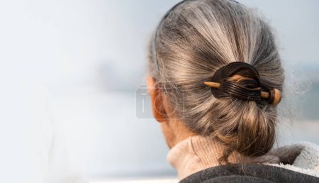 Téléchargez les photos : Une femme aux cheveux gris magnifiquement coiffés, attachée avec une épingle à cheveux, regarde vers l'avenir, une dame âgée prend soin de la santé et de la beauté de ses cheveux et accepte sur sa couleur naturelle. - en image libre de droit
