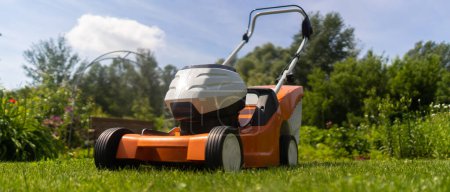 A lawn mower is outside at the beautiful green floral backyard lawn. A lawnmower is cutting a lawn on a summer sunny day.