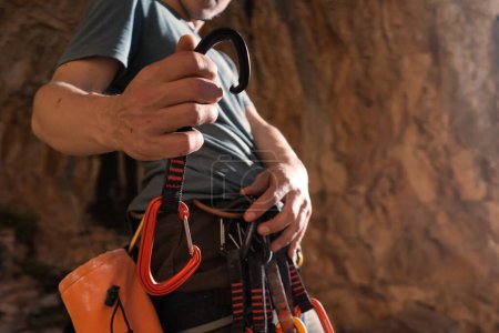 Un jeune homme fort et sportif est engagé dans l'escalade et l'alpinisme, une main d'homme tient un équipement d'escalade, un gros plan rapide sur un fond de rochers rouges par une journée ensoleillée.