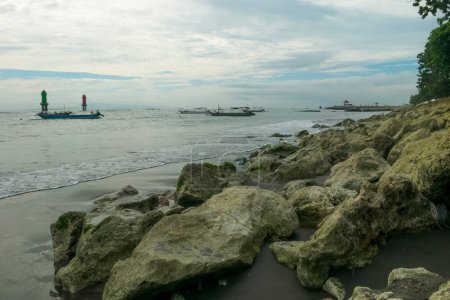 Téléchargez les photos : L'atmosphère le matin à Matahari Terbit Beach, Sanur, Bali, Indonésie. Il y a des vagues qui s'écrasent contre les rochers, les bateaux de pêche et les tours de guet - en image libre de droit