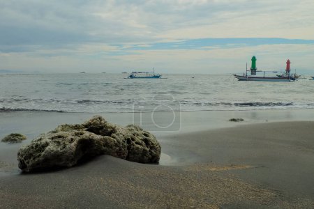 Téléchargez les photos : L'atmosphère le matin à Matahari Terbit Beach, Sanur, Bali, Indonésie. Il y a des vagues qui s'écrasent contre les rochers, les bateaux de pêche et les tours de guet - en image libre de droit