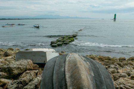 Téléchargez les photos : L'ancienne coque d'un bateau (bateau de pêche) qui s'est échoué sur un tas de rochers de plage, et une vue sur la plage avec un bateau de pêche et une tour de guet - en image libre de droit